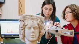澳门金沙线上赌博官网的教授和她的学生正在检查一座古代的半身像雕塑.